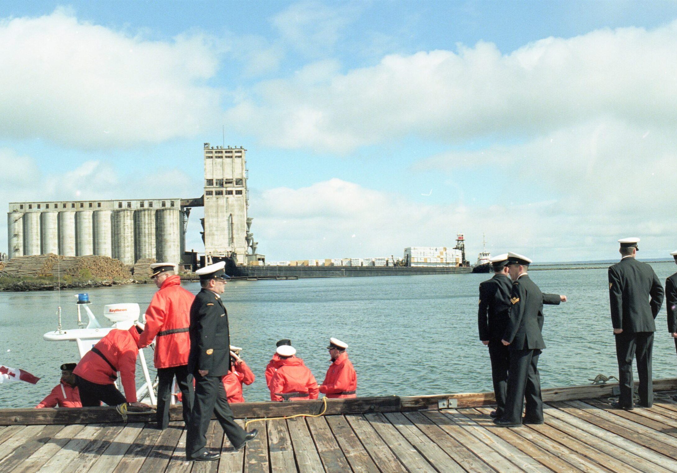 changing of commands on dock - multiple captians and shipmen standing upon the dock with the port and elevator in the background