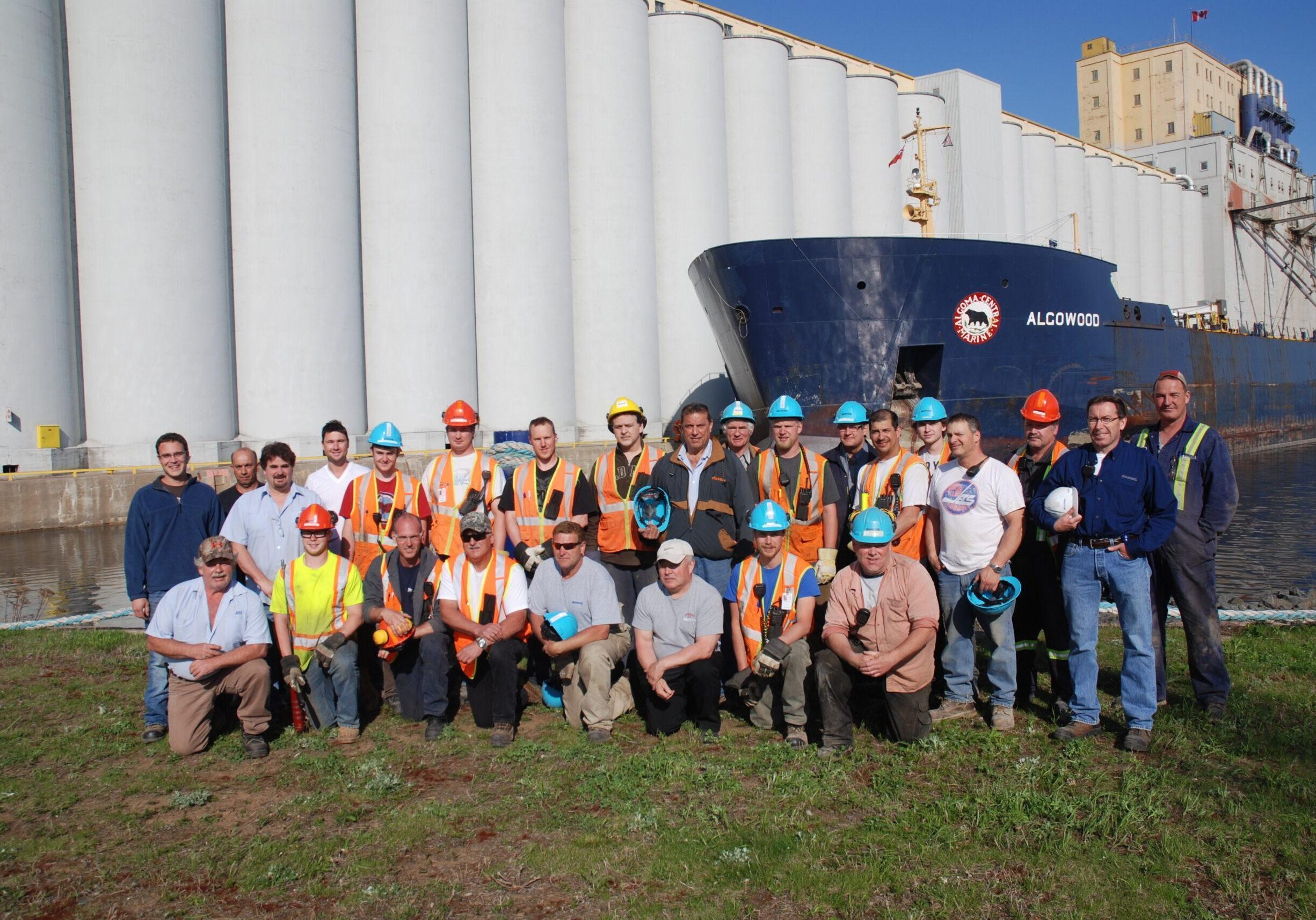 group image of over 20 people with hard-hats on in front of grain elevator