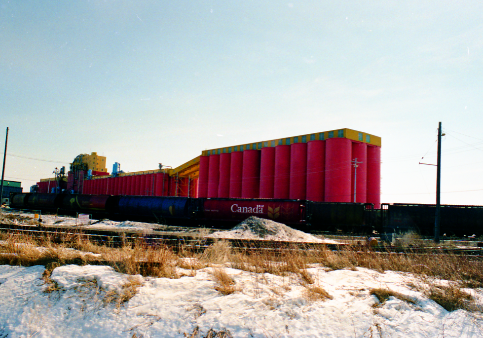 large red elevator with train in front and grass with a bit of snow covering