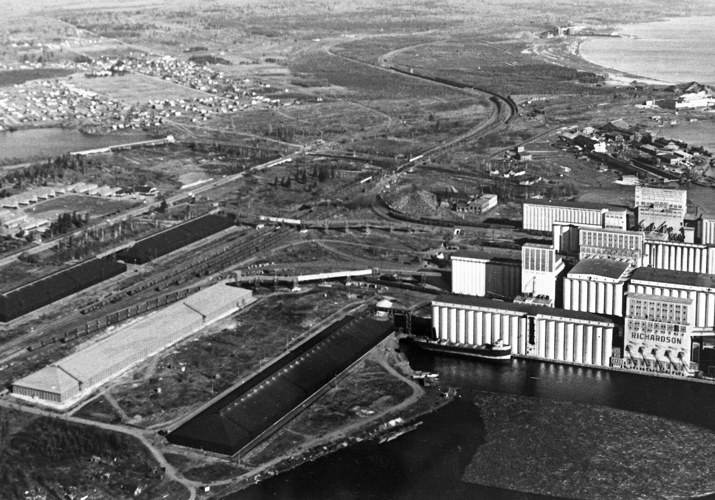 birds eye view of city with relevaotr and lake on the bottom right side of black and white image